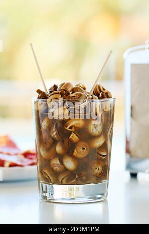 gros plan d'un verre avec caracolillos en caldo, une recette espagnole de petits escargots cuits et servis dans un bouillon typique de l'andalousie, à côté d'une assiette de se Banque D'Images