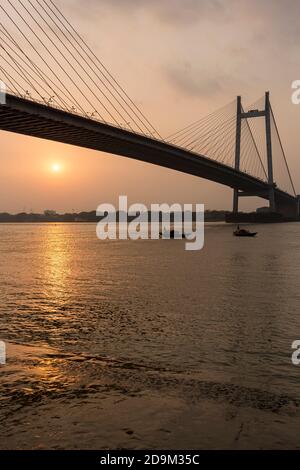 Vue sur le célèbre Vidyasagar Setu sur fond de soleil couchant, bateaux sur la rivière Hoogly. Banque D'Images