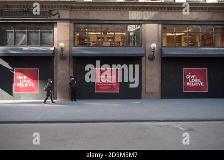 Un agent de sécurité portant un masque se tient devant l'une des fenêtres de Macy. Banque D'Images