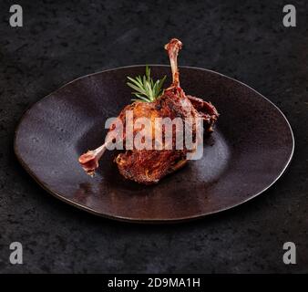 Confite les pattes de canard sur une assiette noire, fond sombre Banque D'Images