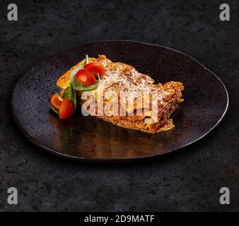 Lasagnes savoureuses à la viande recouverte de fromage servi sur fond noir plaque Banque D'Images