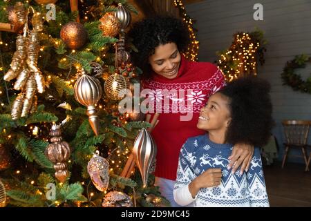 Bonne mère et fille afro-américaine embrassant, décorant l'arbre de Noël Banque D'Images