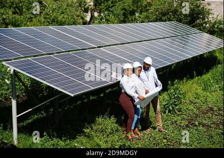 Un technicien afro-américain vérifie la maintenance des panneaux solaires. Groupe de trois ingénieurs noirs réunis à la station solaire. Banque D'Images