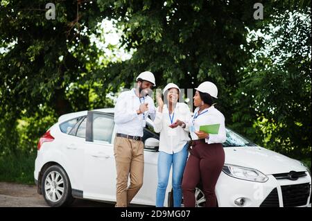 Technicien afro-américain en casques blancs près de la voiture. Groupe de trois ingénieurs noirs. Banque D'Images