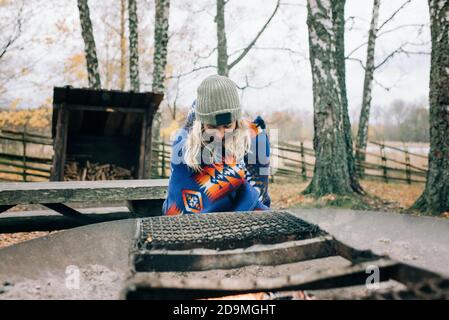 femme assise par un feu de camp enveloppé dans une couverture La forêt en Suède Banque D'Images