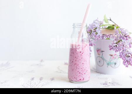 Smoothie de baies dans un pot en verre avec une paille pour des cocktails, branche de lilas dans un seau avec un modèle de femme vélo sur fond léger.régime, detox.refus o Banque D'Images