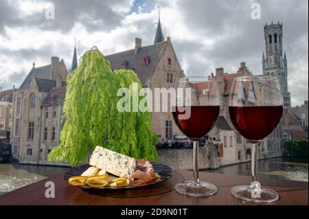 Deux verres de vin avec viande et fromage contre vue sur la vieille ville de Bruges et la tour du Beffroi à Bruges, Belgique. Verre de vin rouge avec différents en-cas Banque D'Images