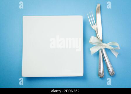 Fourchette d'argent et un couteau avec un ruban blanc et plaque sur fond bleu Banque D'Images