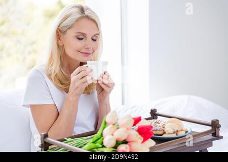 Photo de charmante dame âgée s'asseoir lit blanc linge de boisson odeur de café frais boisson rêveur chambre à l'intérieur Banque D'Images