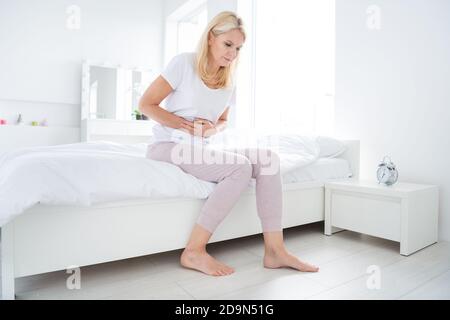 Photo de triste femme pieds nus assis linge de lit le matin souffrir des périodes douloureuses sentir la mauvaise ménopause salle concept à l'intérieur Banque D'Images