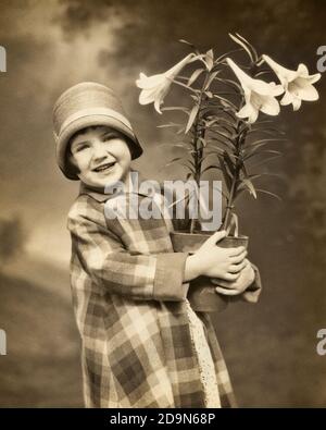 ANNÉES 1920, UNE PETITE FILLE SOURIANTE REGARDANT UN APPAREIL PHOTO PORTANT UN MOTIF ÉCOSSAIS MANTEAU CLOCHE CHAPEAU TENANT UN POT DE LYS DE PÂQUES - E30 HAR001 HARS EASTER STUDIO TOURNÉ MAISON VIE COPIE ESPACE DEMI-LONGUEUR INSPIRATION FESTIVAL CHRISTIAN PLAID SPIRITUALITÉ B&W CONTACT VISUEL BONHEUR GAIE RELIGION CHRISTIANISME CLOCHE FIERTÉ SOURIRES JOYEUSE ÉLÉGANT ET FIDÈLE LYS COOPÉRATION FOI CROISSANCE JUVÉNILES PRINTEMPS CROYANCE BLANC ET NOIR CAUCASIEN ETHNICITÉ HAR001 À L'ANCIENNE Banque D'Images