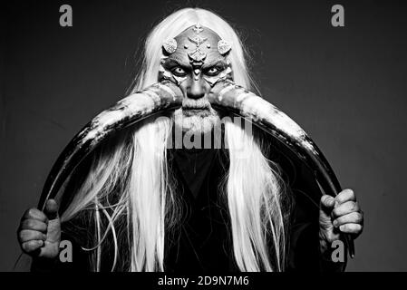 Homme âgé tenant deux cornes rouges. Tête de démon isolée sur noir. Alchimie ancienne. Cornes de diable. Vieux barbu habillé comme un monstre d'Halloween. Druide Banque D'Images