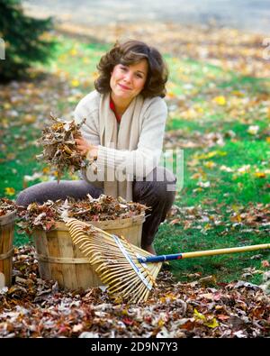 ANNÉES 1980 BRUNETTE FEMME RAKING DES FEUILLES SÈCHES AVEC UNE TENUE DE PEIGNE DE BAMBOU UNE POIGNÉE DE FEUILLES AU-DESSUS DU PANIER SOURIANT EN REGARDANT VERS LE HAUT APPAREIL-PHOTO - KG9594 PHT001 HARS NATURE COPY SPACE DEMI-LONGUEUR DAMES PERSONNES SÈCHES RATISSANT OEIL CONTACT BRUNETTE BONHEUR BAMBOU GAI HAUT LES CORNIÈRES D'AUTOMNE SAISON VERS LE HAUT SOURIRES POIGNÉE JOYEUSE ADULTE MOYEN-ADULTE FEMME AUTUMNAL CAUCASIEN ETHNICITÉ AUTOMNE FEUILLAGE VIEUX MODE Banque D'Images