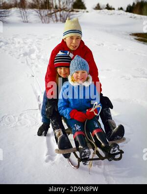 UN GARÇON DES ANNÉES 1960 QUI SE TROUVE SUR UN TRAÎNEAU À NEIGE AVEC SON DEUX SŒURS PLUS JEUNES SOURIANT REGARDANT L'APPAREIL PHOTO, TOUTES EN TRICOT CHAPEAUX DE LAINE - KW2815 HAR001 HARS NOSTALGIE FRÈRE VIEILLE MODE SOEUR 1 FORME PHYSIQUE STYLE JUVÉNILE SAIN TRAVAIL D'ÉQUIPE HEUREUX FAMILLES JOIE STYLE DE VIE FEMMES FRÈRES RURAL TRAÎNEAU SANTÉ MAISON VIE LAINE COPIE ESPACE AMITIÉ DEMI-LONGUEUR HOMMES TOUS LES FRÈRES ET SŒURS SŒURS TRICOTAGE OEIL D'HIVER CONTACT ACTIVITÉ BONHEUR PHYSIQUE GAI GRAND ANGLE AVENTURE SA PROTECTION FORCE EXCITATION RÉCRÉATION FRÈRE SOURIANT SOUPLESSE JOYEUX MUSCLES HIVERNAL CROISSANCE JEUNES PRÉ-ADOLESCENTS PRÉ-ADOLESCENTS GARÇON Banque D'Images