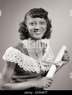 FEMME AFRO-AMÉRICAINE DES ANNÉES 1950 TITULAIRE D'UN DIPLÔME D'ÉTUDES SUPÉRIEURES REGARDANT LA CAMÉRA SOURIRE PORTE FIÈREMENT LA ROBE SUISSE À POIS LACY COL - N705 HAR001 HARS STYLE DE VIE SATISFACTION FEMMES DIPLÔME STUDIO TOURNÉ ESPACE DE COPIE DAMES EXPRESSIONS DE CONFIANCE B&W CONTACT VISUEL OBJECTIFS RÊVES BONHEUR UNIVERSITÉS GAIES LES CONNAISSANCES AFRO-AMÉRICAINES LES CONNAISSANCES AFRO-AMÉRICAINES L'ORIGINE ETHNIQUE NOIRE EST FIÈRE DE SOURIRE ÉDUCATION JOYEUSE LACY LES COLLÈGES ÉLÉGANTS POINTILLÉ SUISSE JEUNE FEMME ADULTE NOIR ET BLANC HAR001 AFRO-AMÉRICAINS À L'ANCIENNE Banque D'Images