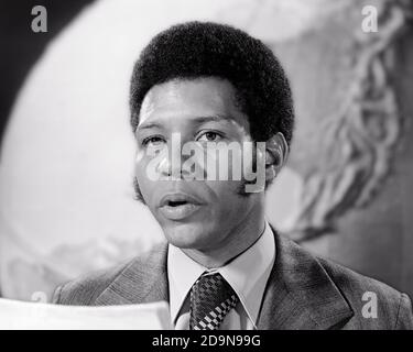 ANNÉES 1970 UN HOMME AFRO-AMÉRICAIN QUI REGARDE UN APPAREIL PHOTO POUR LIRE DES NOUVELLES DIFFUSION AVEC IMAGE D'ARRIÈRE-PLAN GLOBALE - R22515 HAR001 DIFFUSION HARS COPY SPACE PERSONNES AFRO HOMMES PROFESSION CONFIANCE JOURNALISTE B&W EYE COSTUME DE COMPÉTENCES DE CONTACT ET D'ÉGALITÉ COMPÉTENCES D'OCCUPATION TÊTE ET ÉPAULES DIFFUSION DE L'IMAGE GLOBALE AFRO-AMÉRICAINS CARRIÈRES AFRO-AMÉRICAINS EMPLOI NOIRFAIRE DE L'ETHNICITÉ EMPLOI MÉTIERS DE LA CHEVELURE FACIALE ÉLÉGANT EMPLOYÉ JOURNALISME ADULTE MOYEN-ADULTE HOMME FAVORIS CÂBLE NOIR ET BLANC HAR001 AMÉRICAIN À L'ANCIENNE Banque D'Images