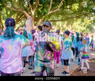 MACKAY, QUEENSLAND, AUSTRALIE - JUIN 2019 : annonceur non identifié avec microphone et couvert de poussière colorée haut fives un entrant dans Color Frenzy Fu Banque D'Images