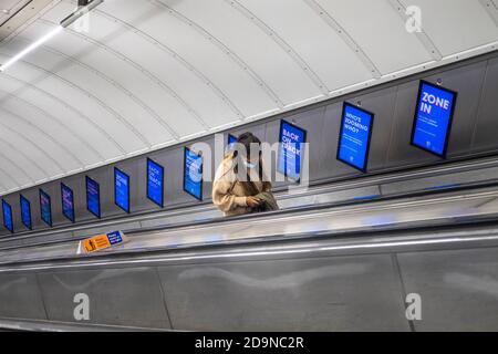 Transport portant un masque facial sur l'escalier roulant dans le métro de Londres, pendant le programme de verrouillage Covid-19 Banque D'Images