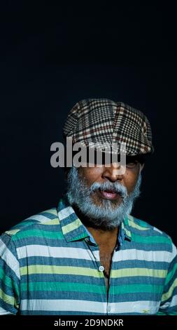 Photo verticale d'un homme asiatique âgé barbu portant un chapeau élégant isolé sur fond noir Banque D'Images