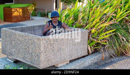 MacKay, Queensland, Australie - 12 juillet 2019 : jeune garçon aborigène assis dans une boîte de jardinières vide souriant la pose des pouces Banque D'Images