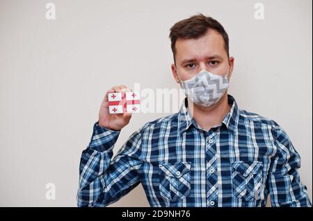 Homme en chemise à carreaux montrer carte drapeau de Géorgie en main, porter masque de protection isolé sur fond blanc. Concept du coronavirus dans les pays asiatiques. Banque D'Images