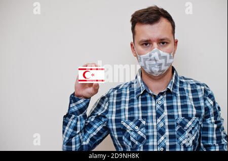 Homme en chemise à carreaux montrer carte drapeau de Chypre du Nord en main, porter masque de protection isolé sur fond blanc. Concept du coronavirus dans les pays d'Europe. Banque D'Images