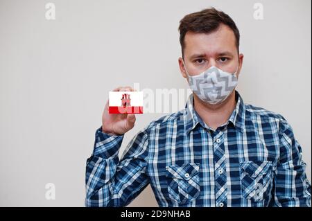 Homme en chemise à carreaux montrer carte drapeau de Gibraltar en main, porter masque de protection isolé sur fond blanc. Concept du coronavirus dans les pays d'Europe. Banque D'Images