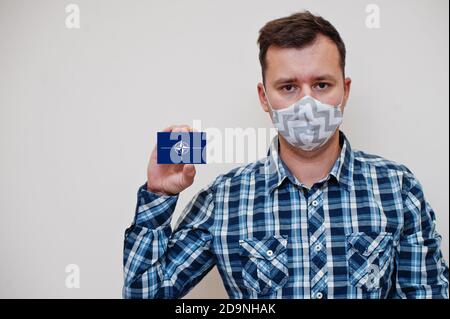 Homme en chemise à carreaux montrer carte drapeau OTAN en main, porter masque de protection isolé sur fond blanc. Concept du coronavirus dans les pays d'Europe. Banque D'Images