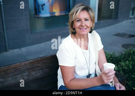 femme assise sur le banc souriante autour d'un café Banque D'Images