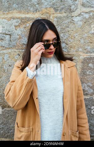 Belle jeune femme posant sur un mur portant des lunettes de soleil Banque D'Images