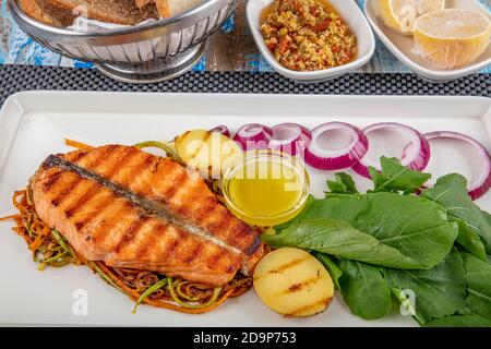 Délicieux filets de saumon cuits. Un morceau de saumon grillé poivre citron et sel sur une assiette blanche avec feuilles de laitue. Fond en bois. Banque D'Images