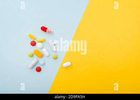Composition médicale. Quelques pilules de couleur sur fond bleu jaune, vue de dessus. Jeu de capsules, médicaments. Banque D'Images