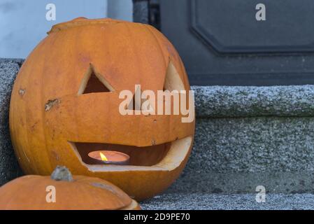 Vue rapprochée de la magnifique citrouille d'Halloween avec bougie allumée à l'intérieur sur les escaliers à côté de la porte. Décoration effrayante et effrayante pour Halloween 2020 Banque D'Images