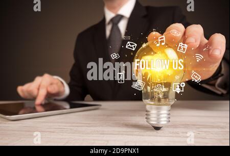 Businessman holding ampoule avec SUIVEZ-NOUS inscription, social media concept Banque D'Images