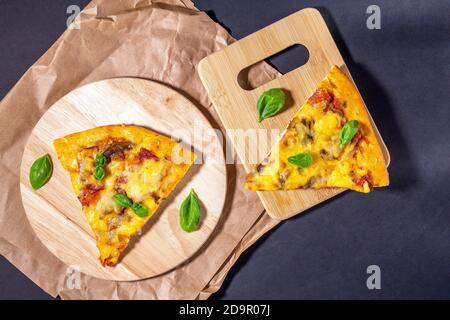 Pizza Basil laisse sur fond noir, vue de dessus. Pizza au jambon, à la viande, au fromage, aux tomates et aux champignons. Deux pièces. Banque D'Images