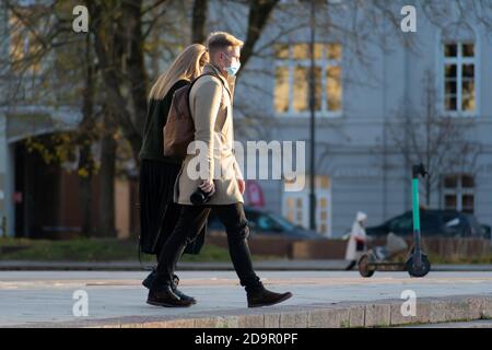 Couple portant un masque et marchant dans la ville avec électrique Trottinette en arrière-plan pendant l'éclosion de Covid ou de coronavirus Banque D'Images
