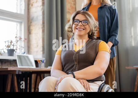 Bonne jeune femme souriante en fauteuil roulant regardant vers l'avant contre elle ami Banque D'Images