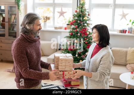 Heureux homme mature passant trois boîtes-cadeaux à sa jolie femme tout en la regardant Banque D'Images