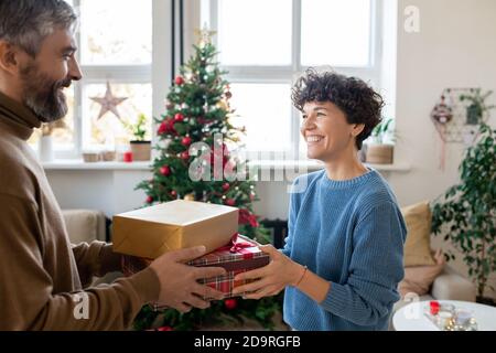 Heureux barbu homme passant deux boîtes-cadeaux à sa jolie femme tout en la regardant Banque D'Images