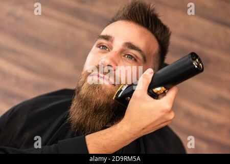 Vue de dessus d'un client dans un salon de coiffure, sa barbe est taillée et coupée avec un rasoir électrique Banque D'Images