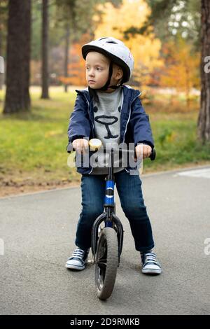 Adorable garçon blond en tenue décontractée et casque de sécurité debout route asphaltée Banque D'Images