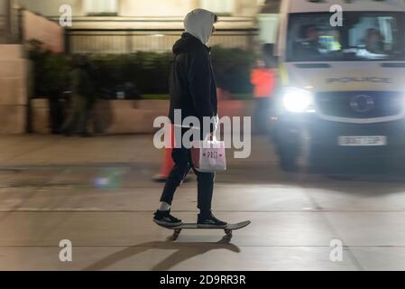Un jeune homme fait du skateboard devant une camionnette de police à Trafalgar Square la nuit, le premier jour du deuxième confinement national de la COVID-19. Skateboarder à Londres Banque D'Images
