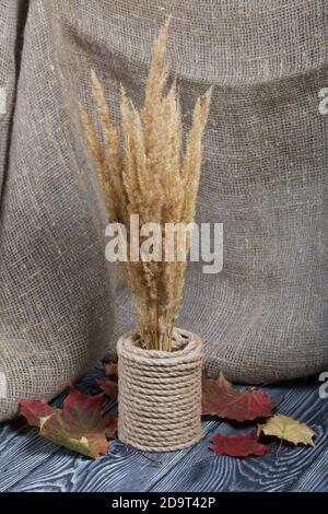 Un bouquet d'herbes sèches dans un bol à ficelle. À proximité se trouvent des feuilles d'automne séchées. Sur le fond de tissu de lin sur les planches de pin. Banque D'Images