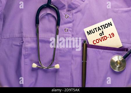 Uniforme médical, carte blanche avec des mots mutation de COVID-19, stylo métallique et stéthoscope. Médecine et concept de pandémie COVID-19. Banque D'Images