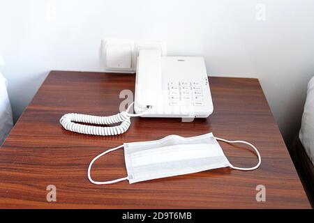 Téléphone et masque médical sur la table de nuit de l'hôtel. Le concept d'une nouvelle réalité et de vacances sûres. Banque D'Images