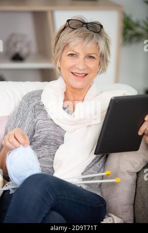 femme âgée utilisant une tablette numérique et tricotage Banque D'Images