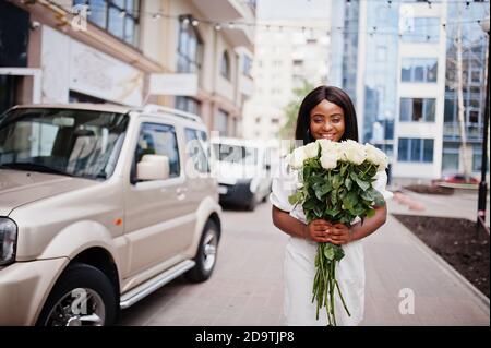 Belle fille afro-américaine tenant bouquet de fleurs roses blanches sur la datation dans la ville. Femme d'affaires noire avec bouquet de fleurs près de la voiture. Banque D'Images