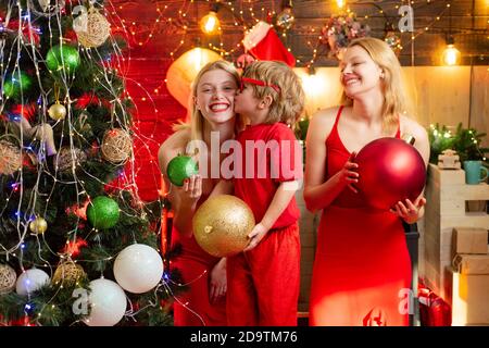 Joyeux Noël à la famille. Deux jeunes filles blondes en robe rouge jouent avec un petit garçon et ont beaucoup de temps. Souvenirs d'enfance. Vacances d'hiver en famille et Banque D'Images