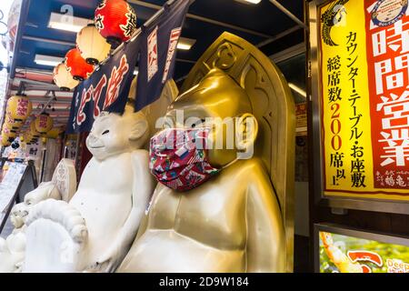 Statue de caractère Billiken devant un restaurant dans la région Shinsekai de Naniwa-ku, Osaka, Japon, portant un masque pendant la pandémie COVID-19 Banque D'Images