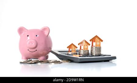 Modèle de maison en bois qui est sur une pile d'argent y compris la banque de porc rose sur fond blanc, l'idée d'économiser de l'argent pour acheter une maison. Banque D'Images